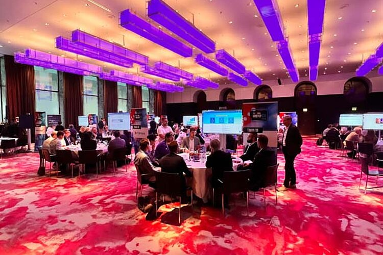 Participants sit at a round table during an ITIL Tool Meetup session, discussing and watching a presentation on a large screen.