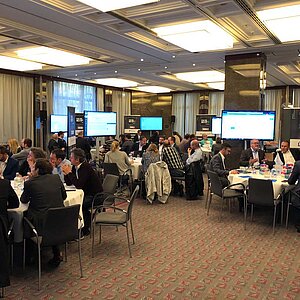 Participants in the ITSM tool MeetUp18 sit at round tables in a modern conference room and discuss IT solutions with experts.