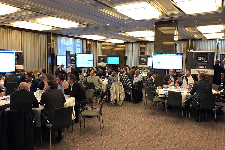 Participants in the ITSM tool MeetUp18 sit at round tables in a modern conference room and discuss IT solutions with experts.
