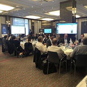 Participants of the ITSM tool MeetUp18 sit at round tables and discuss with manufacturers while presentations are shown on large screens.
