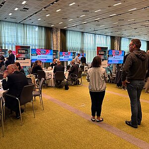 Participants at SERVIEW TOOL MEETUP24 sit at round tables and discuss with manufacturers while presentations are shown on large screens.