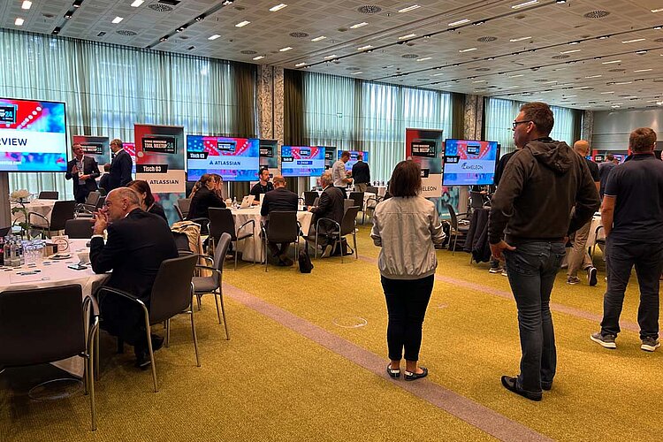 Participants at SERVIEW TOOL MEETUP24 sit at round tables and discuss with manufacturers while presentations are shown on large screens.