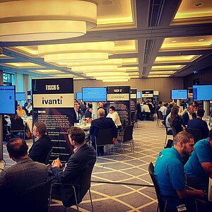 Tool MeetUp participants sit at round tables and discuss with manufacturers while presentations are shown on large screens.