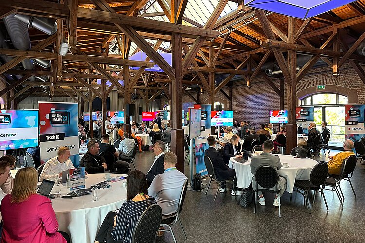 Participants of the SERVIEW TOOL MEETUP23 in a rustic event location with wooden beams and brick walls, discussing at round tables.
