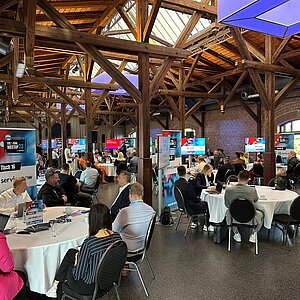 Participants of the SERVIEW TOOL MEETUP23 in a rustic event location with wooden beams and brick walls, discussing at round tables.