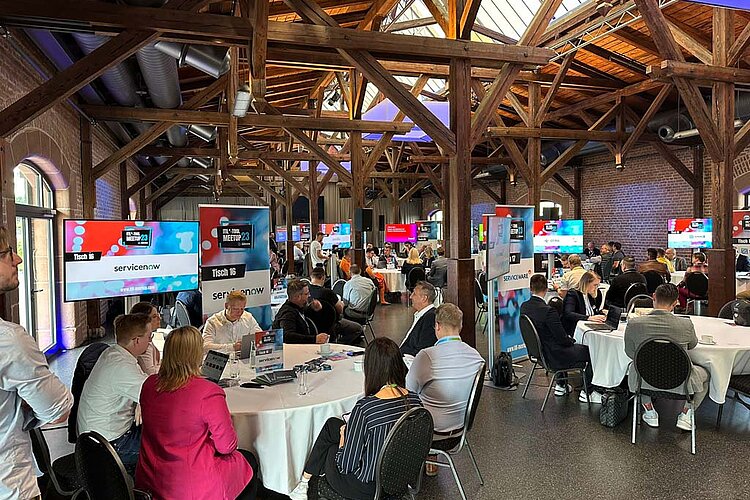 Participants of the SERVIEW TOOL MEETUP23 in a rustic event location with wooden beams and brick walls, discussing at round tables.