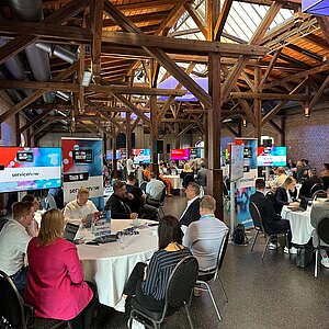 Participants of the SERVIEW TOOL MEETUP23 in a rustic event location with wooden beams and brick walls, discussing at round tables.