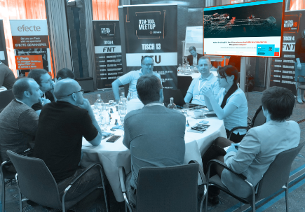 Participants discuss at a round table during a session at the SERVIEW TOOL MEETUP, with a large screen in the background.